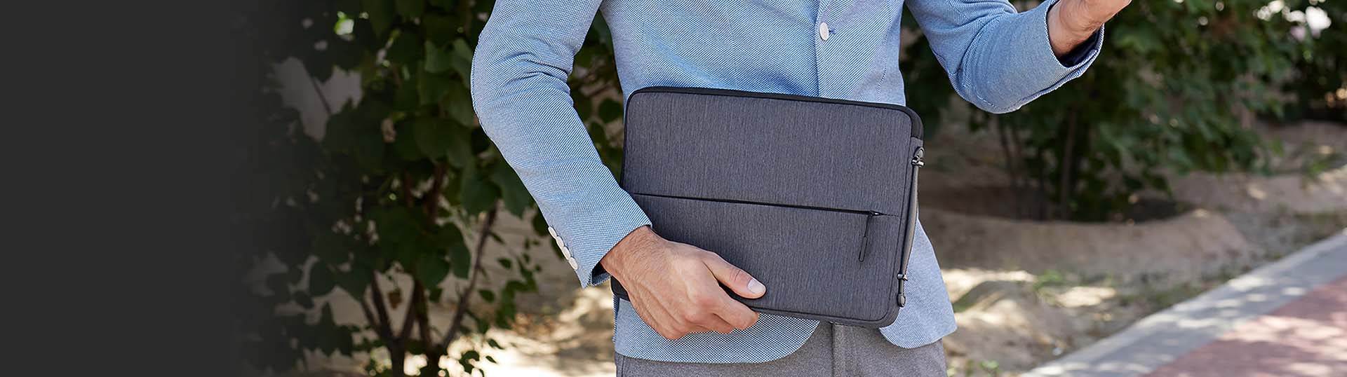 Guy in a light blue suit coat carries a dark gray Lenovo laptop sleeve outside.