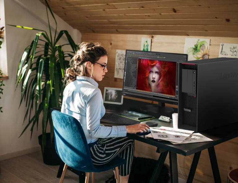 Femme blanche assise à un bureau utilisant la station de travail Lenovo ThinkStation P620 tour pour créer.