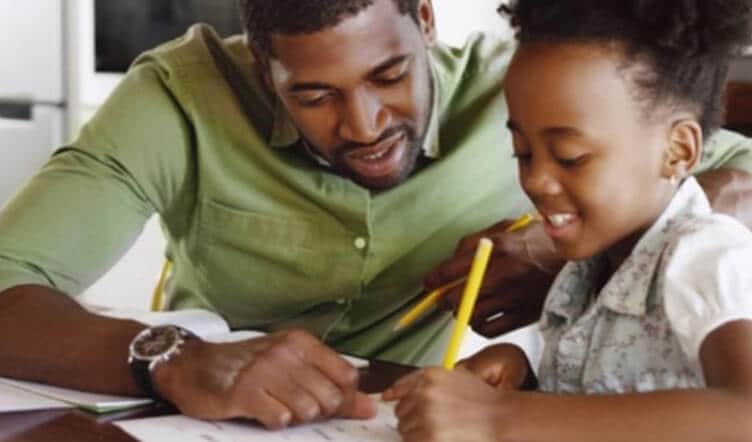 Man/father supervising young girl as she writes on a piece of paper