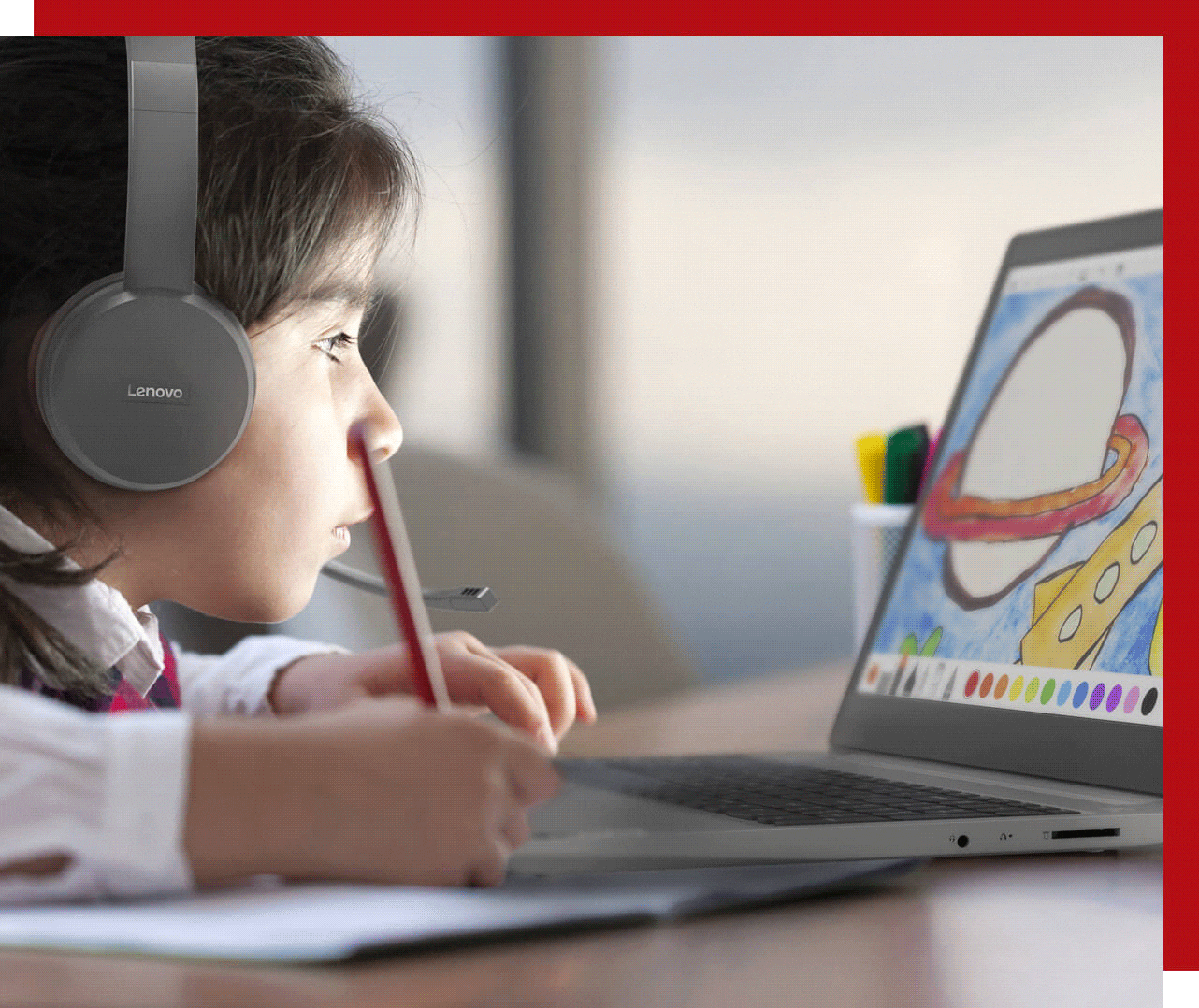 Young boy wearing headphones and working on a drawing app on a Lenovo laptop, showing a planet and a rocket changing colors between red and yellow 