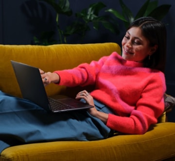 Woman reclining in a large chair with her Lenovo Slim laptop sitting in her lap