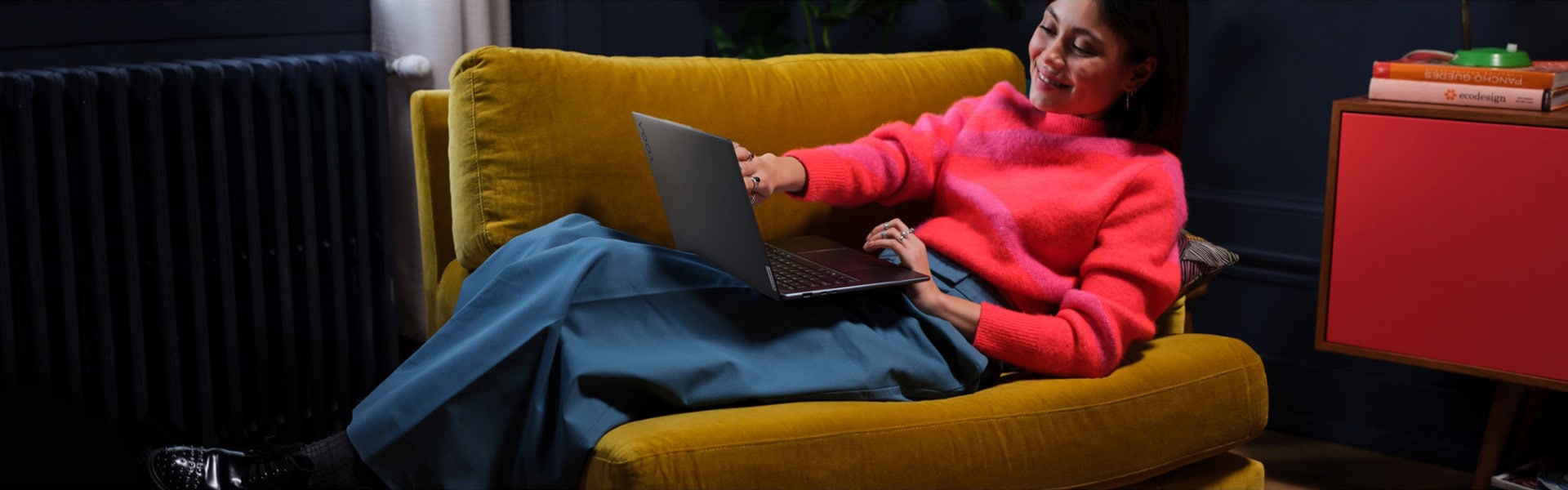 Жена, облегнала се на голям стол, с лаптоп Lenovo Yoga в скута си