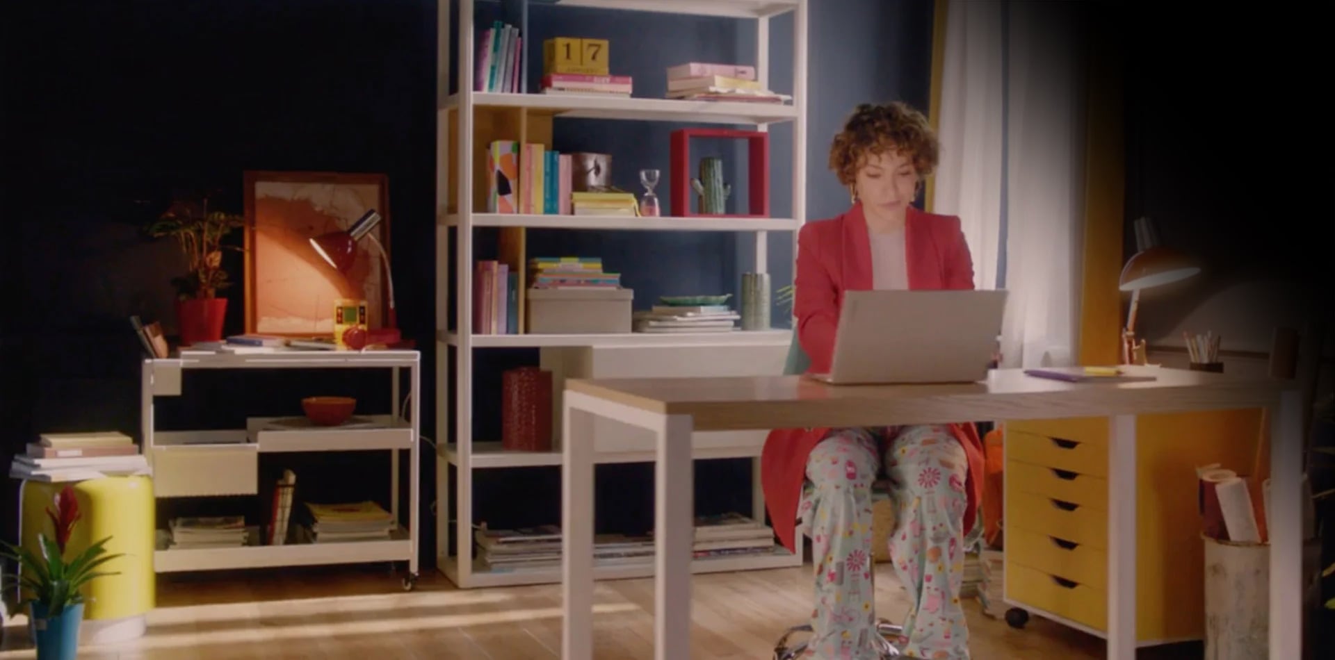 Woman in a suit top and sleep bottoms sitting at a desk with her Lenovo Slim laptop