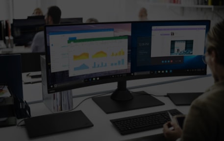 женщина за своим рабочим столом с двумя мониторами, на одном из которых идет встреча по скайпу, а на другом открыты отчет и диаграмма в Excel