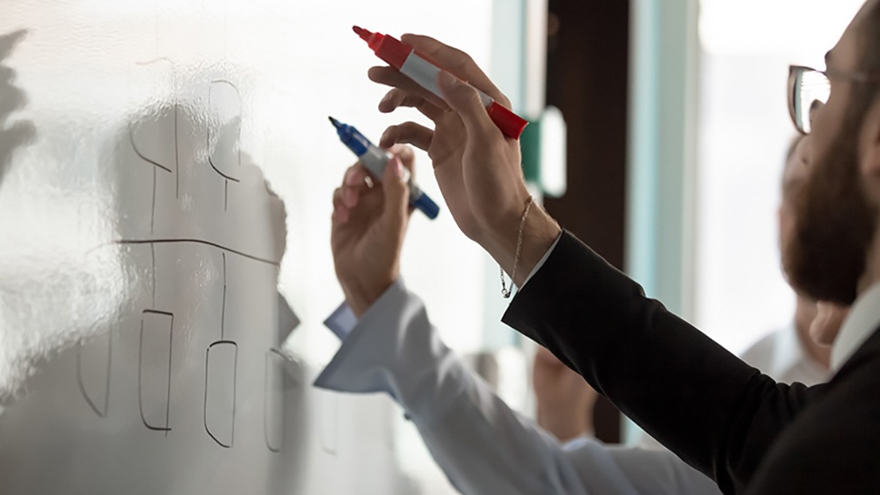 Two people drawing on dry erase board