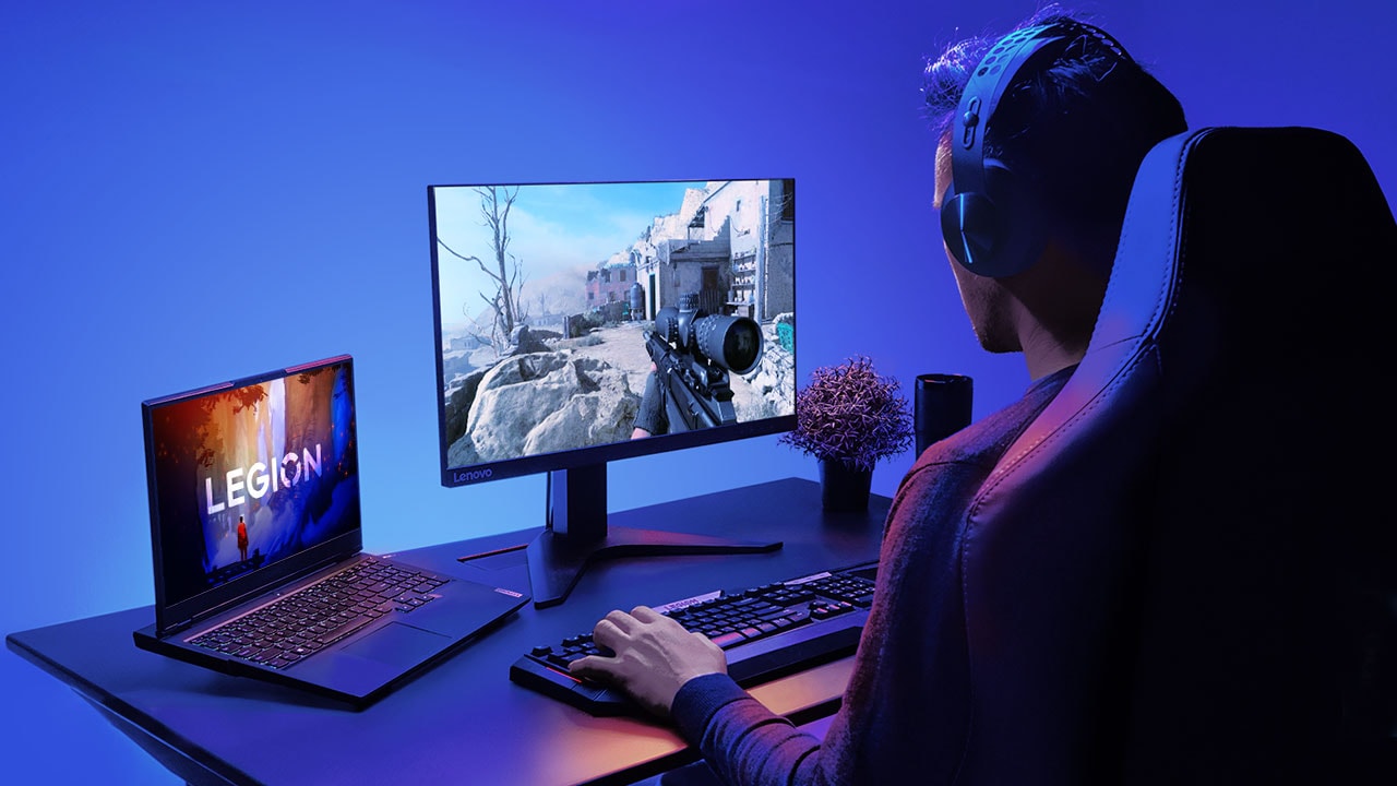 Gamer con cuffie, che gioca su un monitor con un notebook sul lato